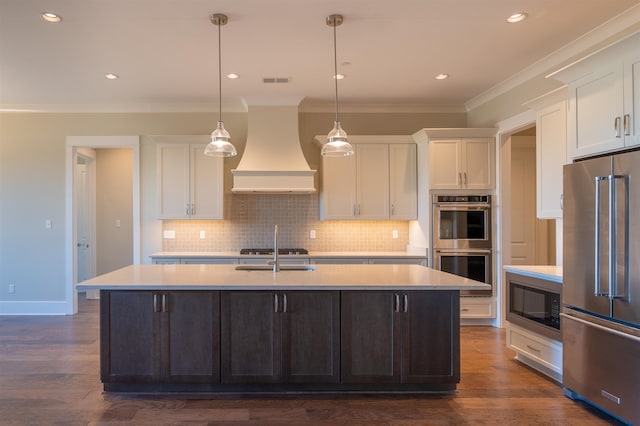 kitchen with appliances with stainless steel finishes, an island with sink, custom range hood, and white cabinets