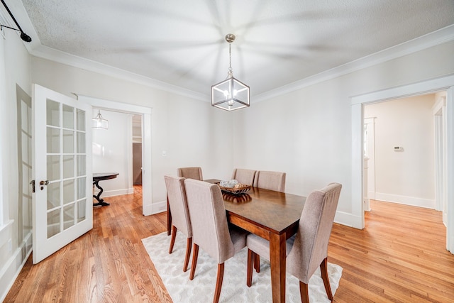 dining space with an inviting chandelier, ornamental molding, a textured ceiling, and light wood-type flooring