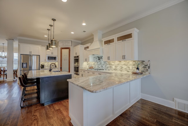 kitchen with premium range hood, decorative light fixtures, a center island with sink, stainless steel appliances, and white cabinets