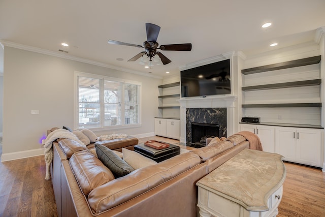 living room with ceiling fan, ornamental molding, a high end fireplace, and light hardwood / wood-style floors