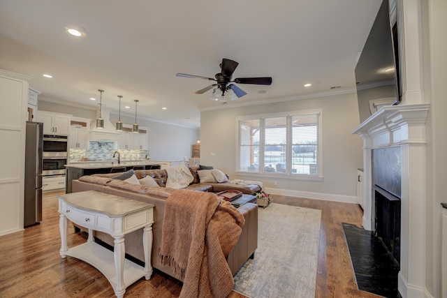 living room featuring hardwood / wood-style flooring, crown molding, ceiling fan, and a high end fireplace