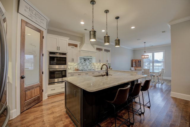 kitchen with sink, white cabinetry, a kitchen island with sink, stainless steel appliances, and light stone counters