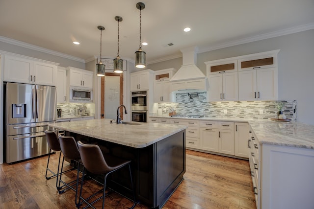 kitchen with white cabinets, stainless steel appliances, custom range hood, and a center island with sink