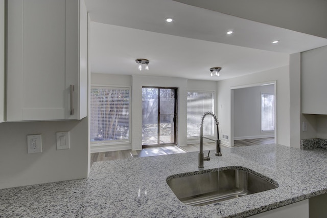 kitchen featuring white cabinetry, sink, light stone counters, and light hardwood / wood-style floors