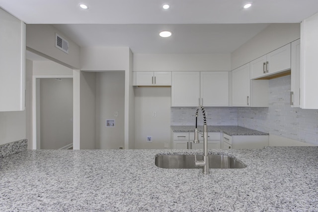 kitchen with tasteful backsplash, light stone countertops, sink, and white cabinets