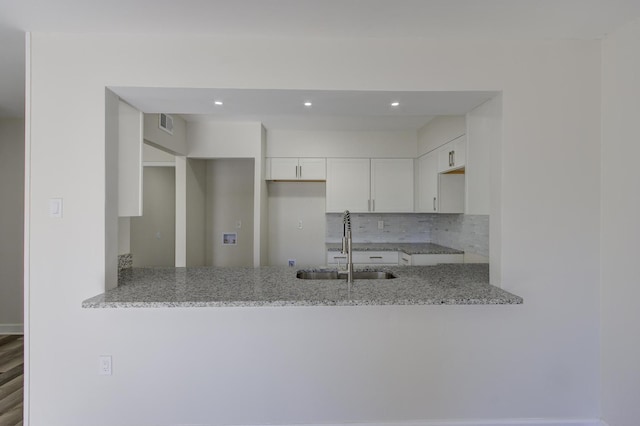 kitchen with light stone counters, sink, backsplash, and white cabinets