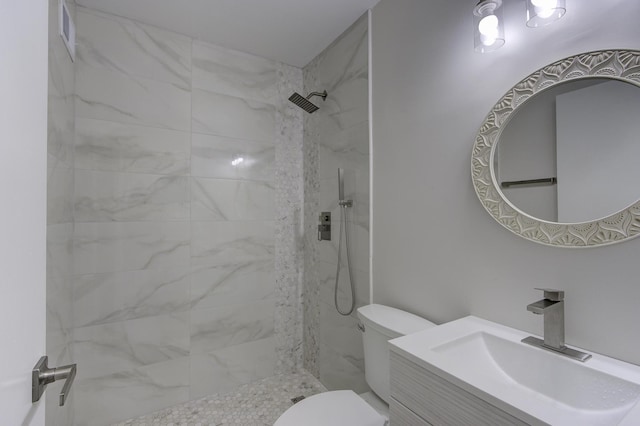 bathroom with a tile shower, vanity, and toilet