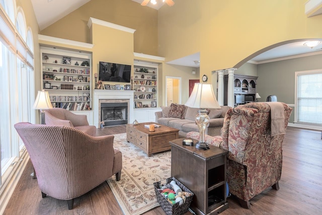 living room with high vaulted ceiling, ornamental molding, built in features, hardwood / wood-style floors, and decorative columns