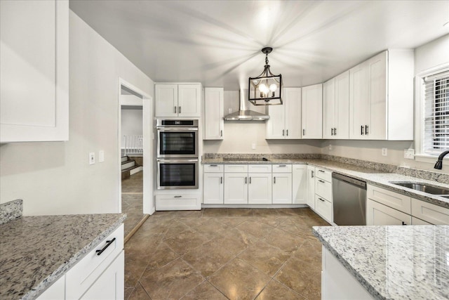 kitchen with wall chimney exhaust hood, sink, white cabinetry, hanging light fixtures, and stainless steel appliances