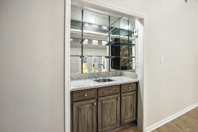 bar featuring light stone countertops, sink, and dark brown cabinetry