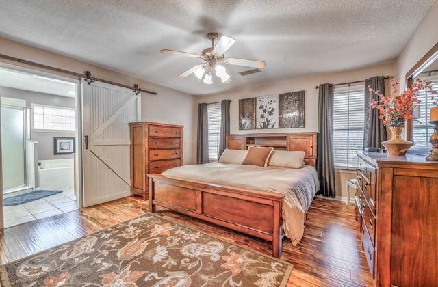 bedroom with ensuite bathroom, a barn door, a textured ceiling, and light wood-type flooring