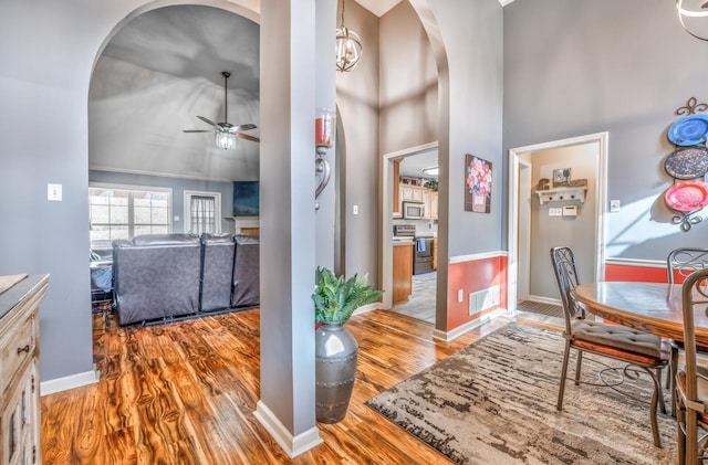 dining space featuring a towering ceiling, ceiling fan, and light wood-type flooring