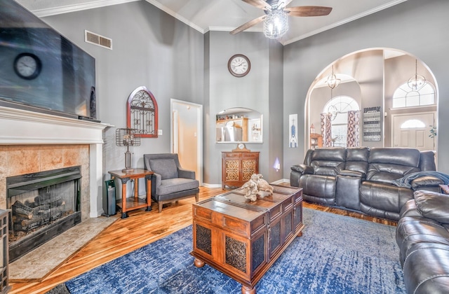 living room featuring crown molding, a tile fireplace, a towering ceiling, hardwood / wood-style flooring, and ceiling fan