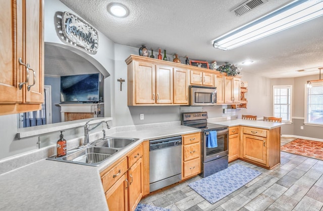 kitchen with appliances with stainless steel finishes, sink, light wood-type flooring, kitchen peninsula, and a textured ceiling