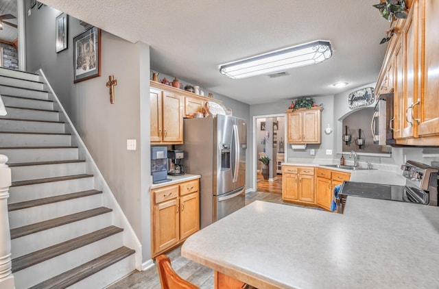 kitchen with light brown cabinetry, sink, kitchen peninsula, stainless steel appliances, and a textured ceiling