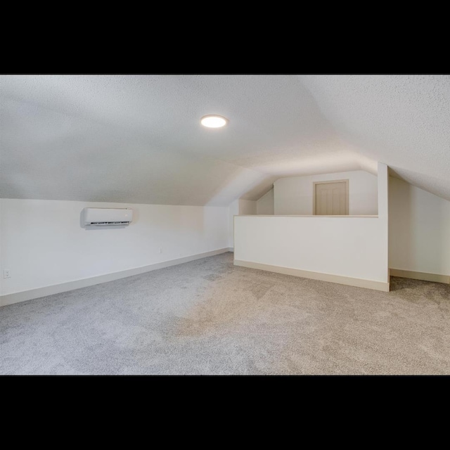 bonus room featuring vaulted ceiling, a wall mounted AC, light colored carpet, and a textured ceiling