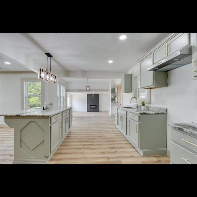 kitchen with decorative light fixtures, sink, a center island, light stone countertops, and light hardwood / wood-style flooring