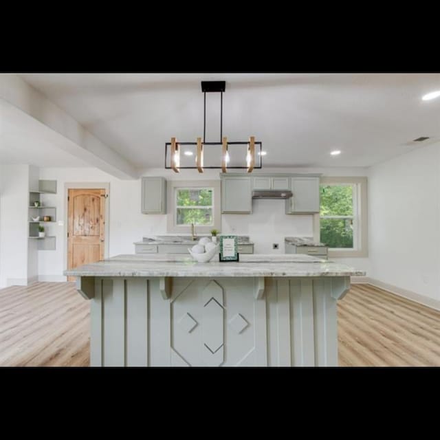 kitchen with gray cabinetry, hanging light fixtures, a large island, light stone countertops, and light hardwood / wood-style floors