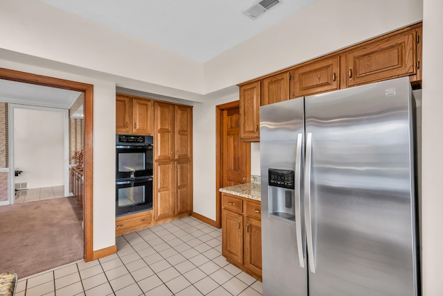 kitchen featuring black double oven, light stone countertops, stainless steel fridge with ice dispenser, and light tile patterned floors