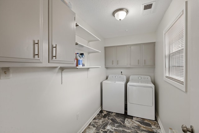 clothes washing area with cabinets, a textured ceiling, and independent washer and dryer