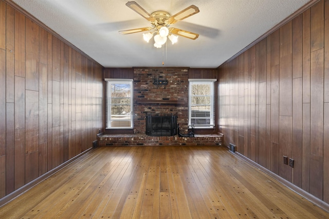 unfurnished living room featuring ceiling fan, plenty of natural light, a fireplace, and light hardwood / wood-style flooring