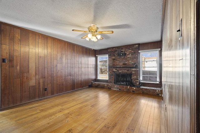 unfurnished living room with a brick fireplace, plenty of natural light, ceiling fan, and light wood-type flooring