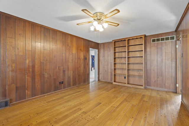 unfurnished bedroom featuring wooden walls, ornamental molding, ceiling fan, and light wood-type flooring