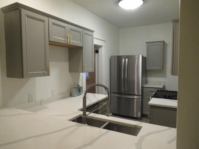 kitchen with stainless steel refrigerator, gray cabinets, sink, and light stone countertops