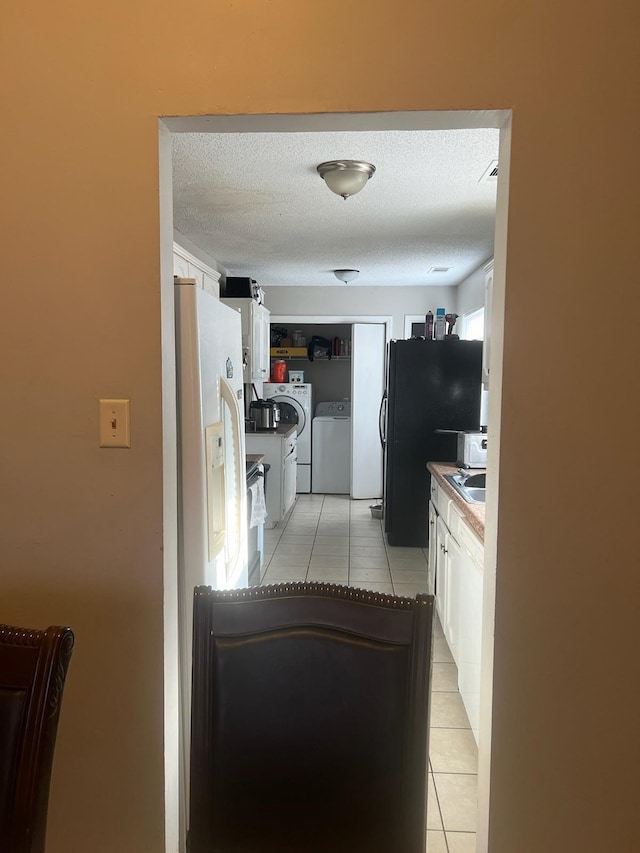 kitchen with a textured ceiling, white cabinets, washing machine and dryer, light tile patterned flooring, and black fridge