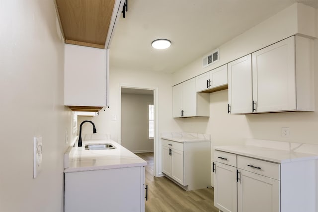 kitchen with white cabinetry, sink, light hardwood / wood-style floors, and light stone countertops