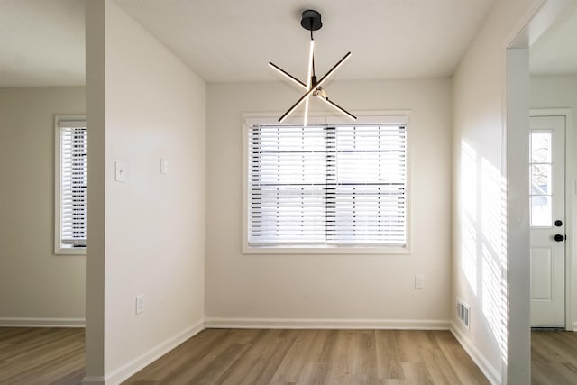 unfurnished dining area with a chandelier and light wood-type flooring