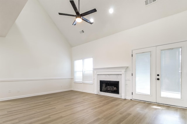 unfurnished living room with french doors, high vaulted ceiling, light hardwood / wood-style flooring, ceiling fan, and a premium fireplace