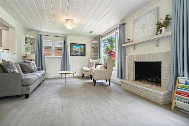 living area with ornamental molding, plenty of natural light, wooden ceiling, and a brick fireplace