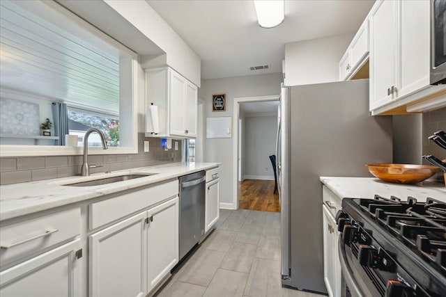 kitchen with sink, light stone counters, appliances with stainless steel finishes, decorative backsplash, and white cabinets