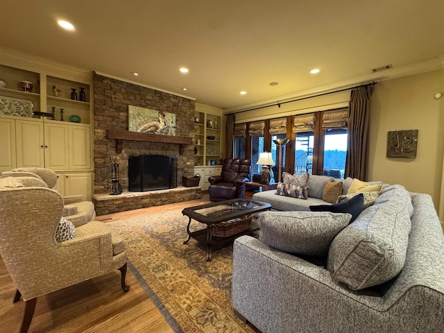 living room featuring crown molding, a stone fireplace, hardwood / wood-style floors, and built in features