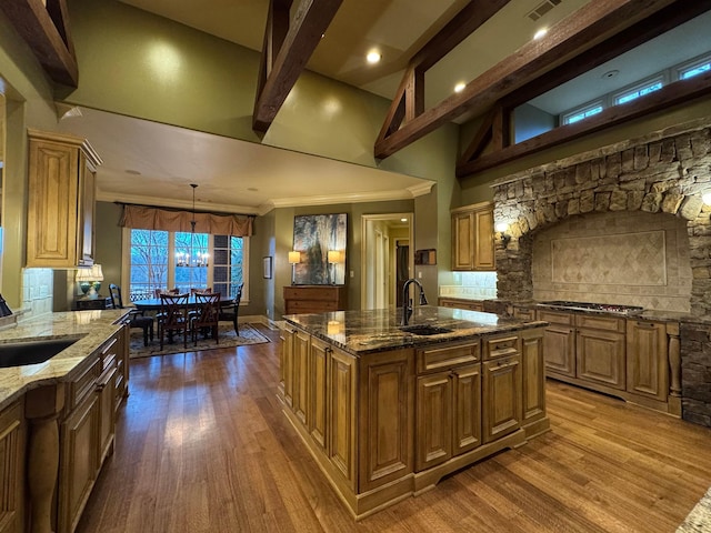 kitchen with stainless steel gas cooktop, dark stone counters, decorative light fixtures, and an island with sink