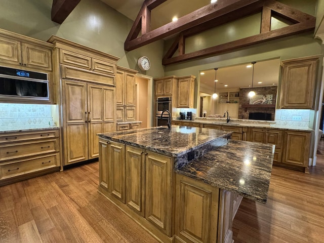 kitchen featuring decorative light fixtures, dark stone countertops, paneled built in refrigerator, a large island with sink, and dark hardwood / wood-style floors