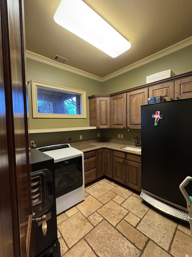 kitchen featuring sink, range, black refrigerator, ornamental molding, and washer / dryer