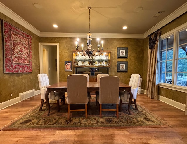 dining space with wood-type flooring, an inviting chandelier, and crown molding