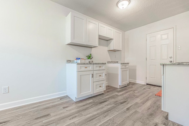 kitchen with a textured ceiling, white cabinets, and light wood-type flooring