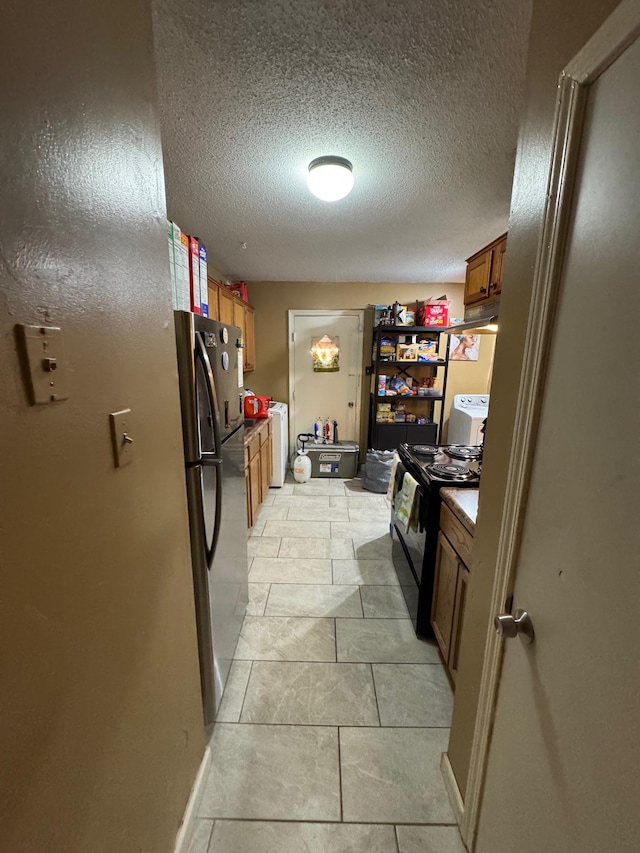 kitchen featuring stainless steel fridge, washer / clothes dryer, black range with electric cooktop, and a textured ceiling