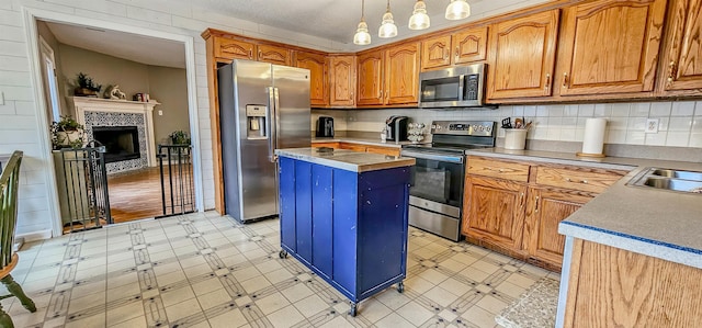 kitchen with pendant lighting, appliances with stainless steel finishes, a center island, a fireplace, and decorative backsplash