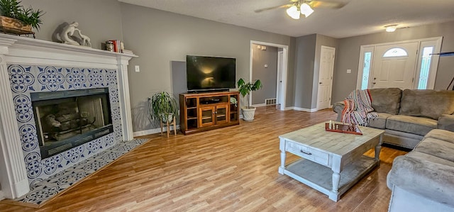 living room featuring a textured ceiling, a fireplace, light hardwood / wood-style floors, and ceiling fan