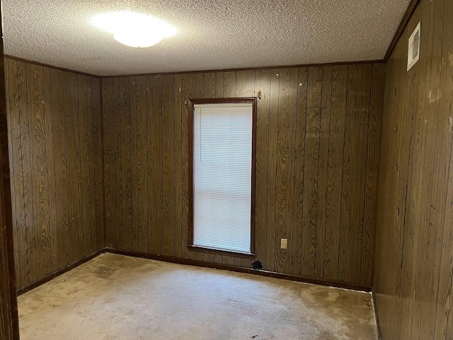 spare room featuring light carpet, a textured ceiling, and wooden walls