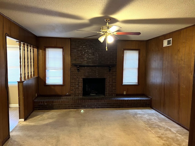 unfurnished living room featuring light carpet, a textured ceiling, wooden walls, ceiling fan, and a fireplace