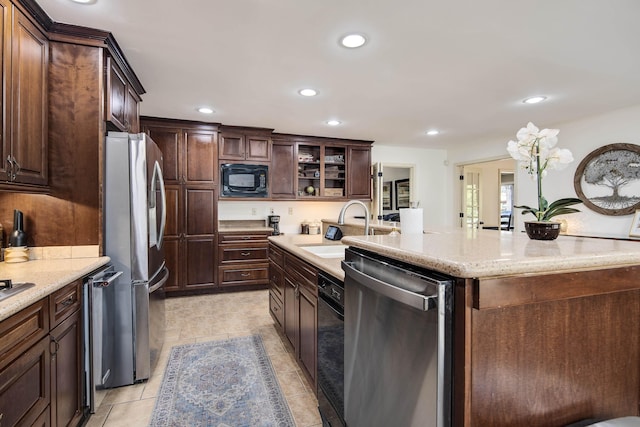 kitchen featuring appliances with stainless steel finishes, sink, a kitchen island with sink, light tile patterned floors, and dark brown cabinets