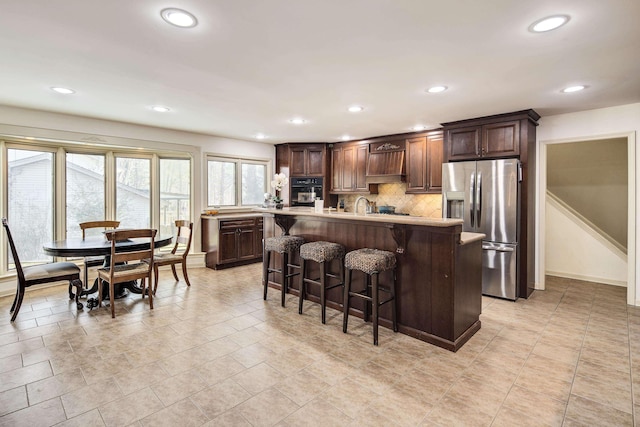 kitchen with a kitchen breakfast bar, a center island, stainless steel refrigerator with ice dispenser, tasteful backsplash, and oven