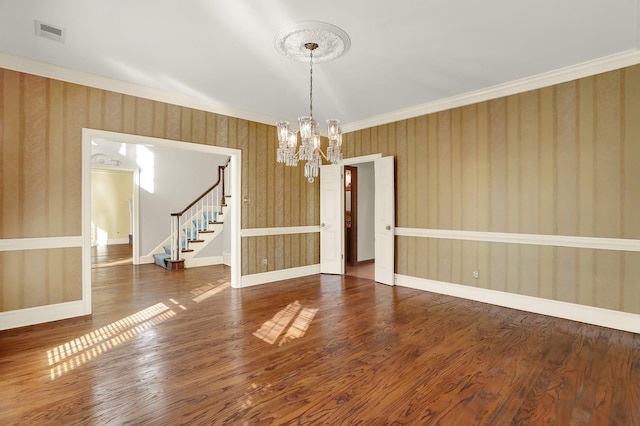 empty room with hardwood / wood-style flooring, ornamental molding, and a notable chandelier