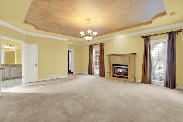 unfurnished living room featuring a chandelier, light colored carpet, a tray ceiling, crown molding, and a brick fireplace