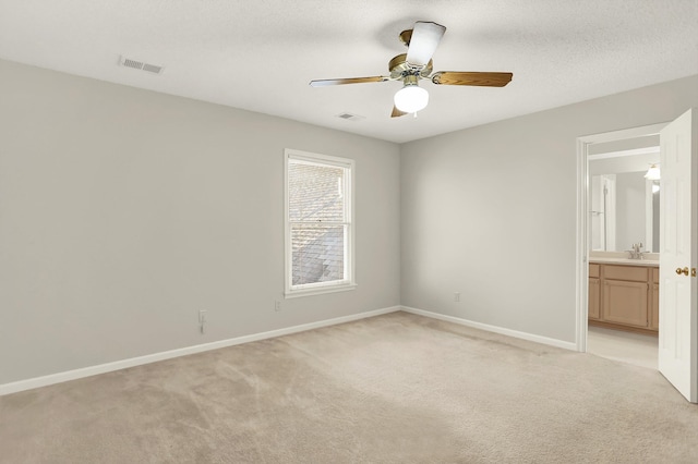 unfurnished bedroom with sink, light carpet, a textured ceiling, and ensuite bath